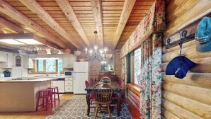 Interior de una cabaña de madera con comedor, cocina y un ventanal grande.