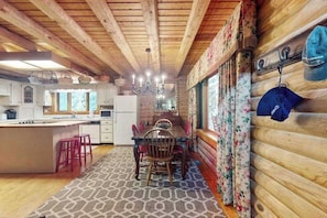 A wooden cabin interior with a dining area, kitchen, and a large window.