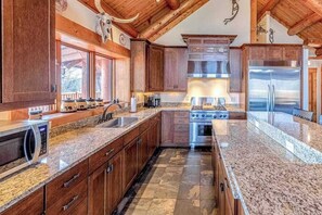 A kitchen with wooden cabinets, granite countertops, a stainless steel refrigerator, and a built-in oven. - Mountain-view log home with hot tub, firepits, pool table & air hockey (Franklin)