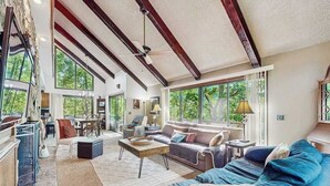 Ein großzügiger Wohnraum mit einer großen Couch, einem Couchtisch und einem Kamin. Große Fenster sorgen für natürliches Licht und einen Blick ins Freie.
