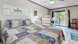 Ein Schlafzimmer mit einem großen Bett, einem Deckenventilator, einem Spiegel, einer Kommode und Blick ins Freie.