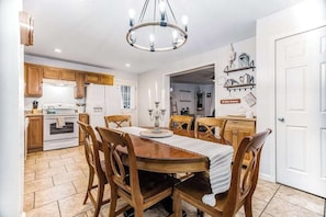 Eine Küche mit Holzausstattung, einem Esstisch mit Stühlen, einer Chandelüster und einem Kühlschrank.