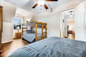 Ein Zimmer mit Etagenbett, einem großen Bett, einem Deckenventilator, einem Fenster mit Aussicht und einer Tür zu einem anderen Raum.