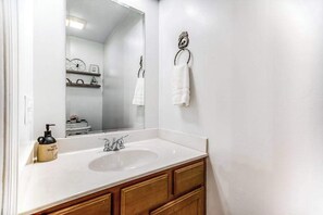 Ein Badezimmer mit einem weißen Waschbecken, Holzschränken, einem Spiegel und einem Handtuchhalter.