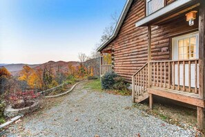 Eine Blockhütte mit Veranda, einem Kiesweg und Blick auf Herbstlaub.