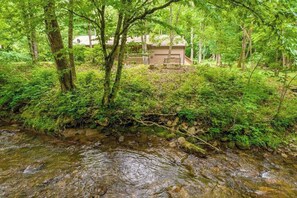 Ein bewaldetes Gebiet mit einem Bach, einer Holzbrücke und einem Gebäude mit Zäun.