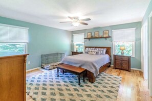 Ein Schlafzimmer mit Bett, Schreibtisch, Stuhl, Deckenventilator und Fenster.
