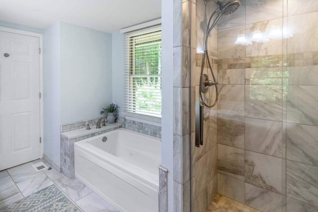 Un baño con bañera, ducha y ventana con persianas.