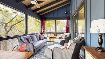 Une pièce chaleureuse avec un plafond en bois, de grandes fenêtres, des meubles en osier et une table.
