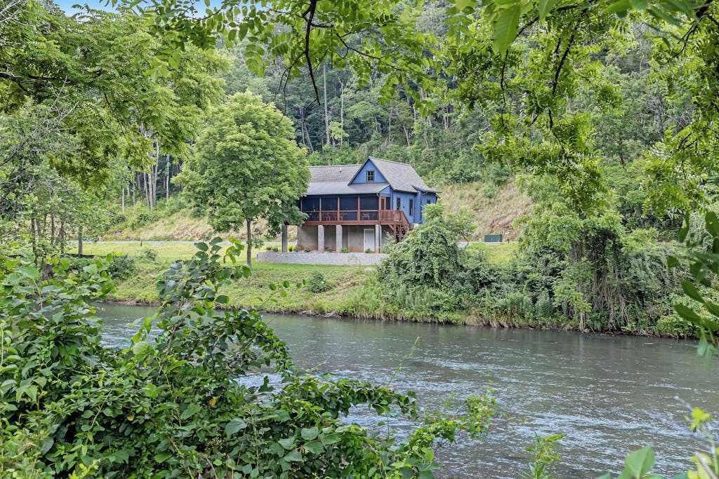 Une maison située au bord d’une rivière, entourée de verdure.