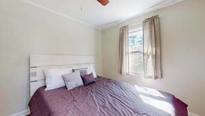Une chambre à coucher avec un lit, une fenêtre avec des rideaux et un ventilateur de plafond.