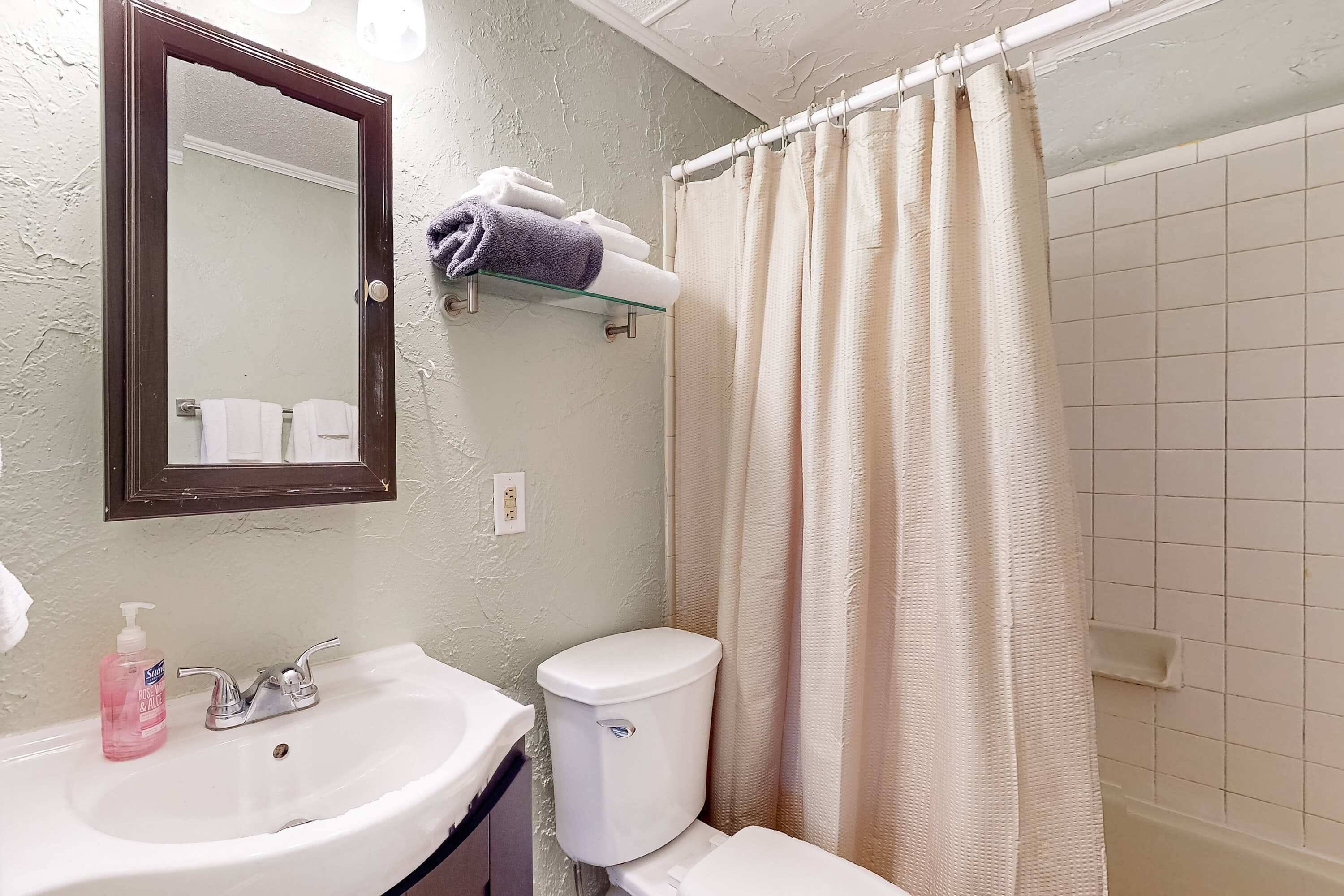A bathroom with a white sink, a mirror, a toilet, and a shower curtain.