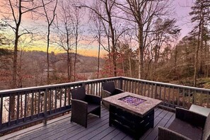 Una terraza con mobiliario de mimbre y una mesa cuadrada, rodeada de árboles y vistas al paisaje.