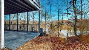 Un espace extérieur abrité, doté d’une terrasse en bois, d’un mur en pierre et offrant une vue sur des arbres et une étendue d’eau.