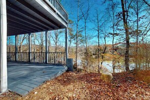 Un espace extérieur abrité, doté d’une terrasse en bois, d’un mur en pierre et offrant une vue sur des arbres et une étendue d’eau.