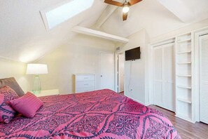 Une chambre à coucher avec un lit, un ventilateur de plafond, une télévision et un placard avec des étagères.