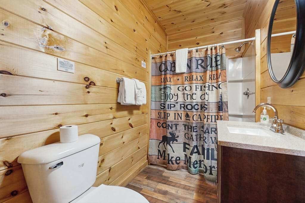 Baño de cabaña de madera con inodoro, lavabo y cortina de ducha con un mensaje motivacional.