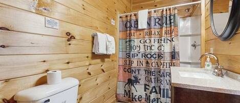 Baño de cabaña de madera con inodoro, lavabo y cortina de ducha con un mensaje motivacional.