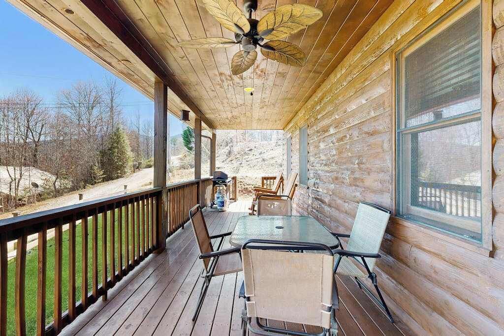 A wooden deck with a table and chairs, a ceiling fan, and a view of a mountainous landscape.