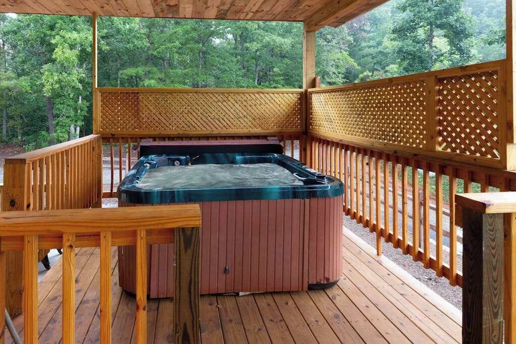 Un jacuzzi en una terraza de madera con barandilla de celosía, rodeado de árboles.