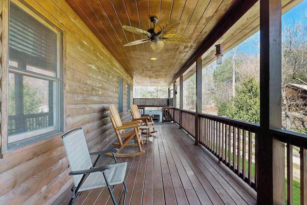 A wooden cabin with a porch, rocking chairs, and a ceiling fan.