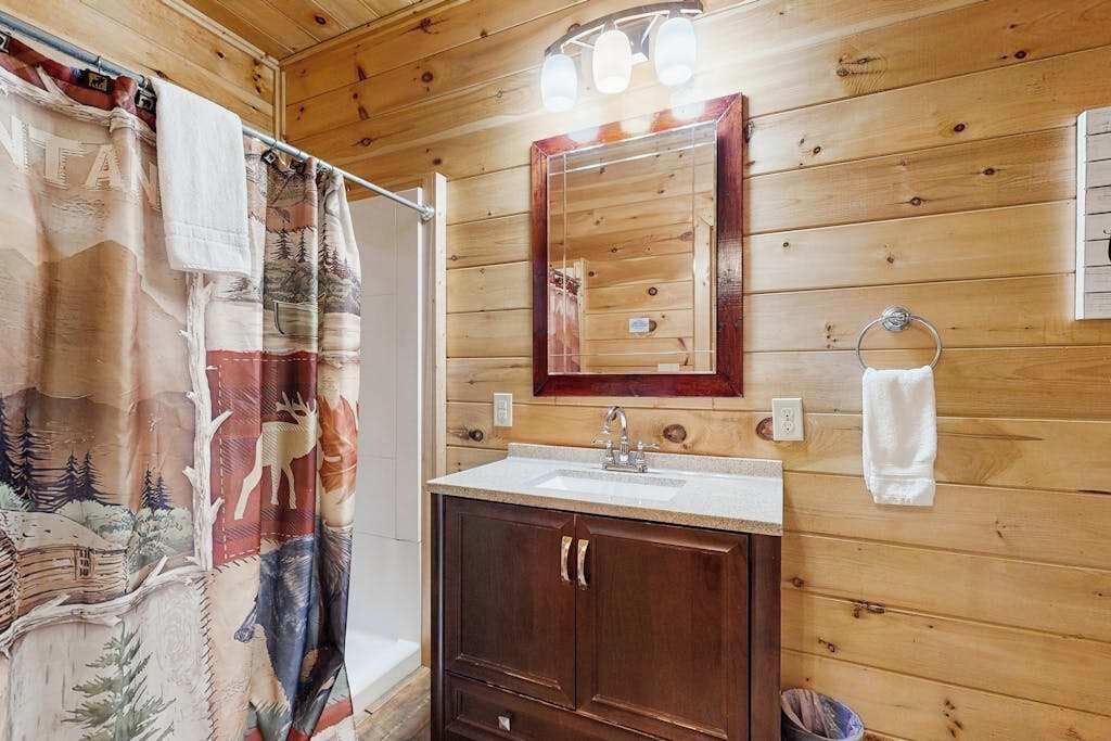 Een houten badkamer met een wastafel, spiegel en douchegordijn.