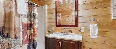 Een houten badkamer met een wastafel, spiegel en douchegordijn.