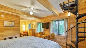 A wooden cabin with a bed, a desk, a chair, a TV, and a staircase. - Chalet at Peek's Creek (Franklin)