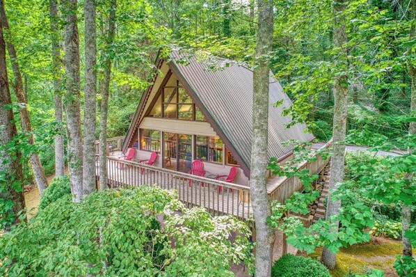 Eine Holzhütte mit einer Holzdachterrasse, großen Fenstern und einer Treppe zum oberen Stockwerk.
