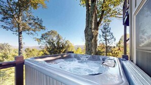 A hot tub on a deck with a view of trees and mountains.