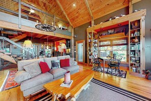 Ein geräumiger Loft mit hoher Decke, freiliegenden Holzbalken, einem großen Sofa, einer Essecke und einem Bücherregal.