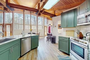 A kitchen with green cabinets, a dishwasher, an oven, and a large window overlooking a forest. - Two-story, dog-friendly home with two kitchens, central AC, & gas fireplaces (Franklin)