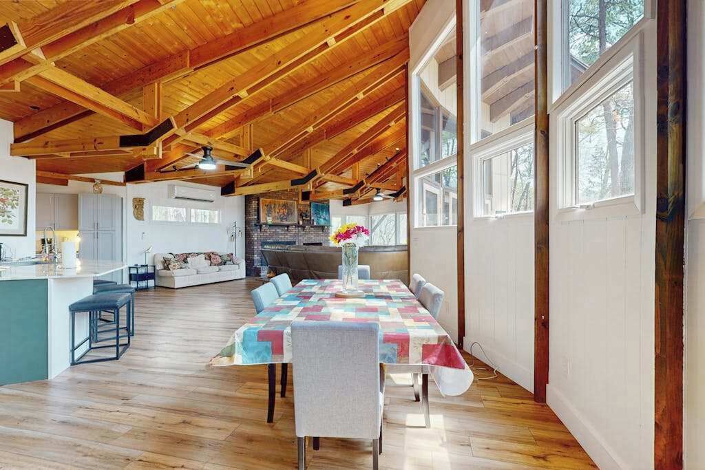Una habitació àmplia amb sostre de fusta, una llarga taula de dinar i una cuina visible a través d'una porta oberta.