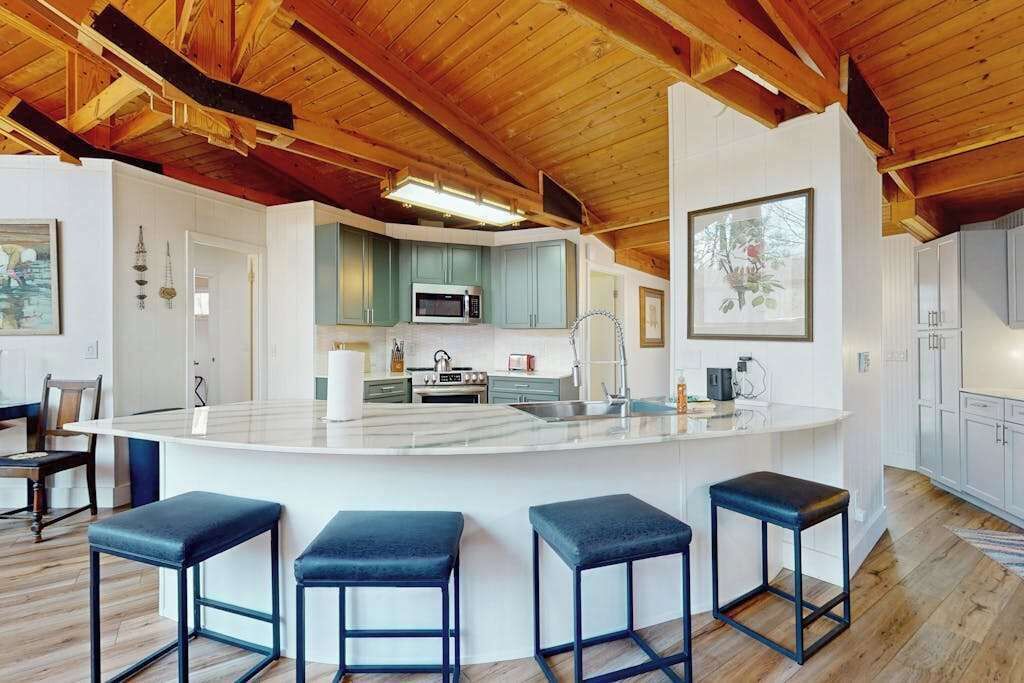 Une cuisine moderne avec un îlot central, des tabourets de bar et des poutres en bois au plafond.