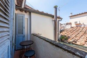 Ein Balkon mit Tür, zwei Stühlen und Blick auf terrakottafarbene Dächer.