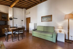 Ein Wohnzimmer mit Holzboden, einem grünen Sofa, einem Esstisch mit Stühlen, einer Uhr und einem Gemälde an der Wand.