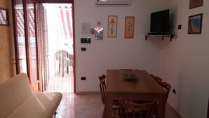 Uma área de refeições com uma mesa e cadeiras, um sofá, um aparelho de ar condicionado e obras de arte fixadas na parede.