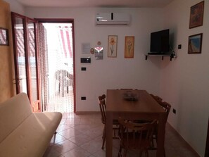 A dining area with a table and chairs, a sofa, an air conditioning unit, and wall-mounted artwork. - Apartment MOON DROP TWO at 300mt. sand (Lido Marini)