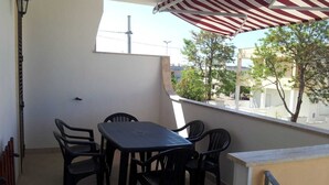 Uma varanda com mesa e cadeiras, um candeeiro e vista para edifícios e árvores.