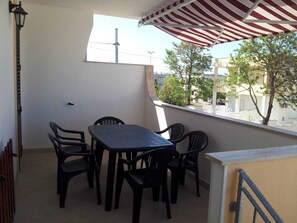 A balcony with a table and chairs, a lamp, and a view of buildings and trees. - Apartment MOON DROP TWO at 300mt. sand (Lido Marini)