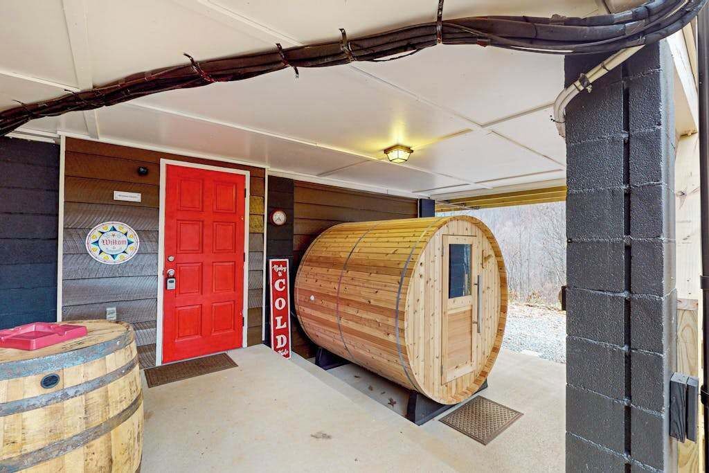 Una sauna con forma de barril de madera, una puerta roja y un cartel que dice 'COLD'.