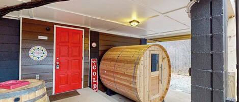 Una sauna con forma de barril de madera, una puerta roja y un cartel que dice 'COLD'.