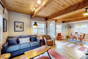 Ein gemütliches Wohnzimmer mit Holzbalkendecke, einer Couch, einem Couchtisch und einem Essbereich mit Stühlen und Tisch.