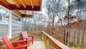 Puinen terassi, jossa on kaksi punaista Adirondack-tyylistä tuolia, ikkuna ja näkymä metsään.
