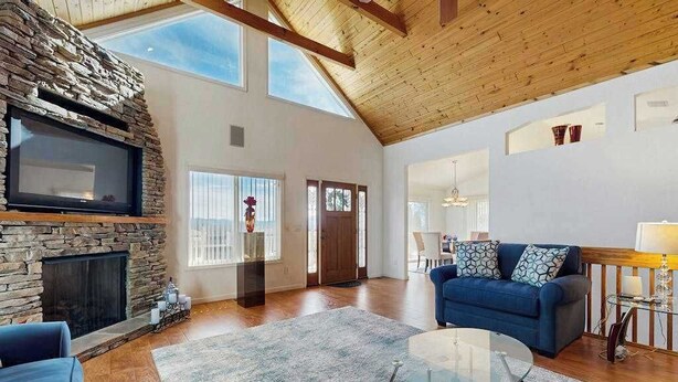 Un salón amplio con chimenea de piedra, un sofá azul, una mesa de centro de vidrio y techo de madera.