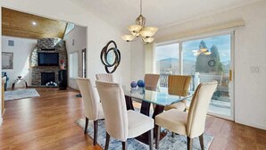 Un comedor con mesa y sillas de vidrio, chimenea de piedra y vistas a través de amplios ventanales.