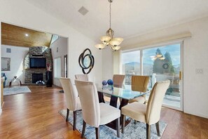 A dining area with a glass table and chairs, a stone fireplace, and a view through large windows. - The Overlook Upper Retreat (Franklin)