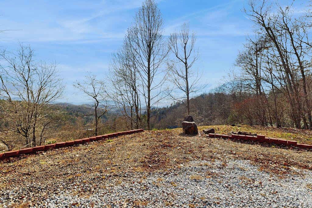 Ein Kiesgrundstück mit einem Metallzaun und einer Steinstruktur, umgeben von baumlosen Bäumen und einer hügeligen Landschaft.