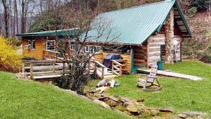 A rustic cabin with a green roof, wooden deck, and a small porch. - Crackerbox Palace (Sylva)