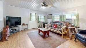 A living room with a television, sofa, coffee table, and a ceiling fan. - Crackerbox Palace (Sylva)
